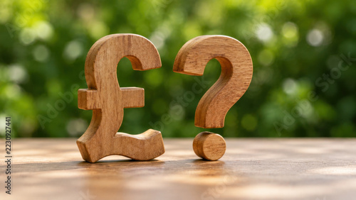 Wooden pound sterling symbol and question mark on table with blurred green garden background, representing financial uncertainty and currency doubt