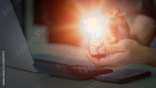 Businessman holding glowing light bulb with laptop computer on desk for bright idea, startup vision, and creative thinking concept.