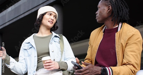 Diverse friends sitting and talking at building entry, wearing jackets, holding coffee, phone, keys
