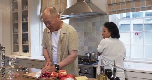 Senior couple cooking together in kitchen, chopping vegetables and stirring pot, at home