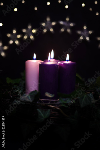 Cozy Advent arrangement: Lit purple and pink candles in a natural wreath, Christmas time.