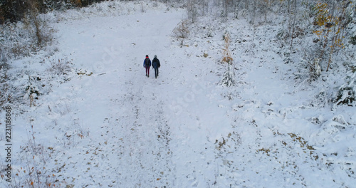 Two people are walking on a snow-covered path in a wintry landscape, with copy space
