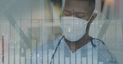 Analyzing healthcare worker wearing scrubs and mask reviewing data charts in clinic
