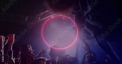 Pulsing neon pink ring above crowd with smartphones at club, with singer in denim reaching mic
