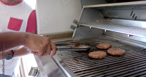 Grilling burgers on barbecue grill, person using tongs for flipping patties