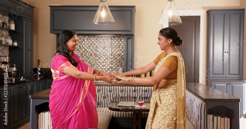Indian mother and teenage daughter in traditional Indian sari dancing and smiling in modern kitchen