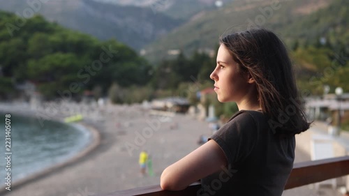 Young woman watching sailboat on calm coastal bay at sunset behind