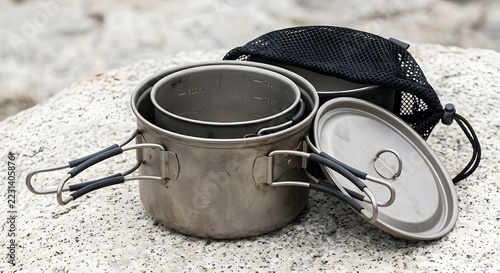 Lightweight titanium camping cookware set with nesting pots and foldable handles on a rock background.