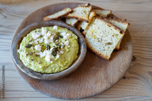 Asparagus and pea dip with feta cheese, served with crispy bread on a wooden platter.