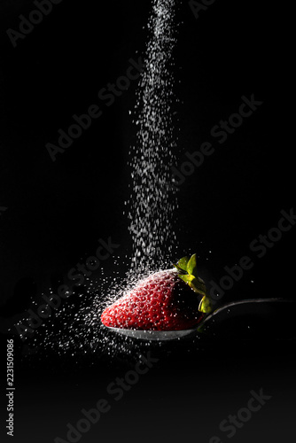Strawberry on a Spoon with Falling Sugar on Black Background