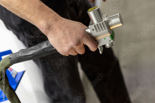 Handheld laser welding gun torch head with copper nozzle and red guide beam close-up.