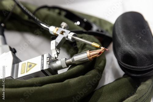 Handheld laser welding gun torch head with copper nozzle and red guide beam close-up.