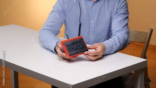 Person in a blue shirt holding a red portable cassette player with a visible tape and headphone cable over a white table, evoking retro music listening and analog audio nostalgia