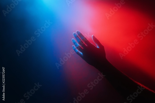 Hand reaching into vibrant red and blue light, creating a powerful, dramatic gesture that conveys energy, tension, and intensity in a visually striking scene.