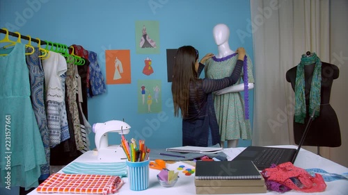 Successful entrepreneur happily working on her upcoming designer dress - Fashion studio. Young fashion designer doing designing work on a dummy and noting down the important details in her laptop 