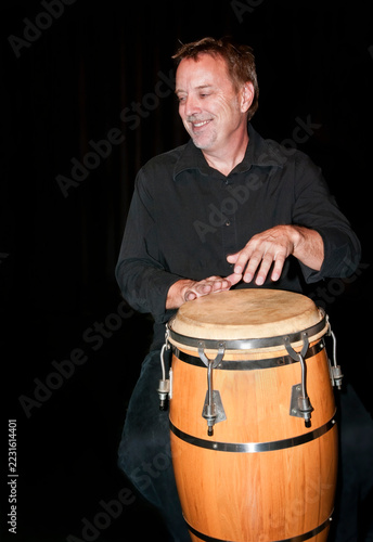 Obraz na plátně Percussionist playing a conga drum against a black background.