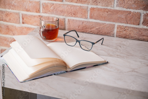 a cozy scene featuring a cup of tea a notebook and glasses on marble table 