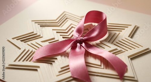 Pink satin ribbon bow on layered paper geometric star background