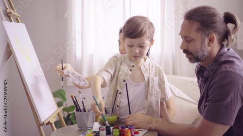 Family guiding little boy painting on canvas easel in cozy room
