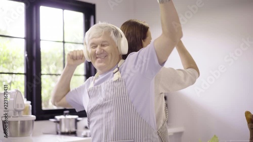 Happy senior couple wearing aprons dancing together in modern kitchen
