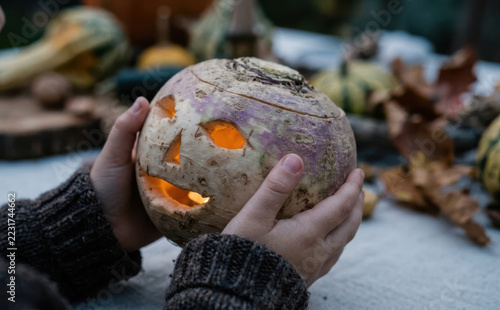 Child holding glowing carved turnip lantern for traditional Halloween celebration outdoors in autumn