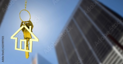 Dangling gold house-shaped keychain with metal keys on ring, catching city towers, copy space