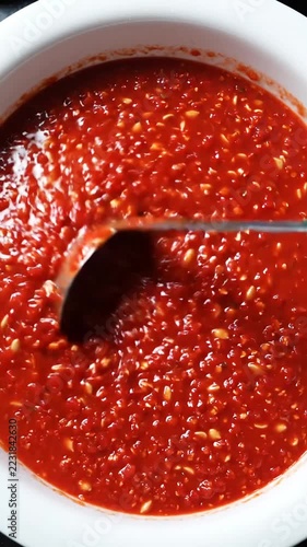 Red chili sauce in a white bowl with a spoon, macro close-up showing bubbling and thick liquid motion