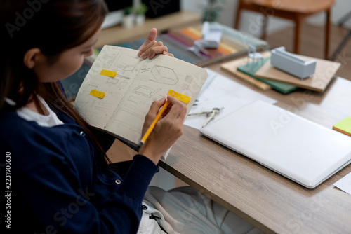 Female Furniture Designer Reviewing Sketches with Yellow Sticky Notes at Office Workspace Desk