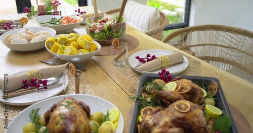 Whole roasted chickens are resting on dark pan on wooden dining table, garnished with lemon