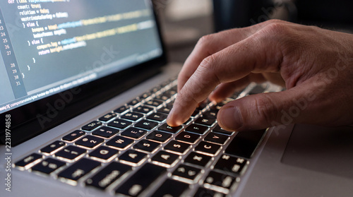 Screen displaying source code, a programmer is typing on the laptop keyboard. Computer language, technology software update, software as service, IT support.