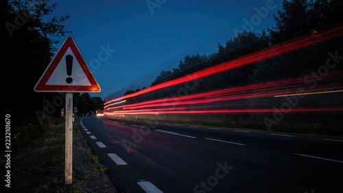 Warning sign on a dark road with red car light trails at night