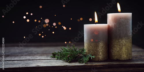 Minimalist christmas decoration featuring two burning candles on rustic wood and magical lights. Horizontal background with copy space.