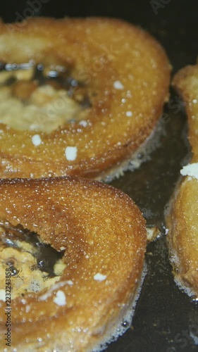 Vertical macro close-up of golden fried bread slices sizzling in hot oil on a pan.