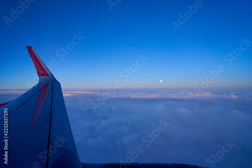 Airplane wing while flying on high cloud and moon on sky to travel destination.