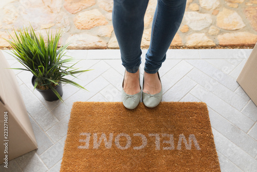 Woman standing near welcome mat in front of door at home