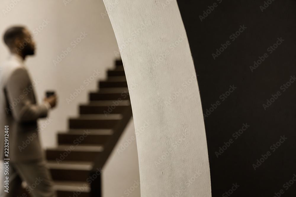 Fototapeta premium A man stands near a staircase next to a large white architectural column in an indoor, minimalist setting.
