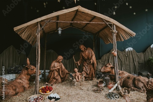 Fotografie A traditional nativity scene display featuring wooden statues of Joseph, Mary, and baby Jesus in a thatched stable with animals and starry background