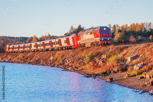 Passenger train moves along the lake.
