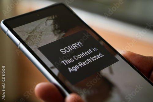 Mobile phone screen showing an alert of age-restricted content to protect minor from mature materials. Close-up, selective focus.