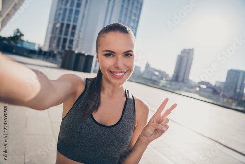 Portrait of sporty lady online blogging crossfit practicing make selfie v-sign outdoors