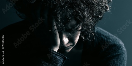 Person sits withdrawn in visible depression. Stark emotional portrait represents isolation, low mood and the burden of mental illness.