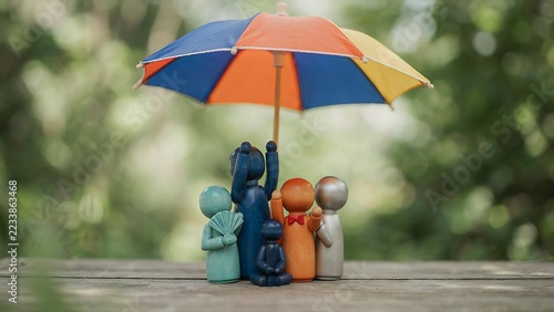 Close up on colorful wooden peg family holding hands and sheltering under rainbow paper umbrella outdoors, created with generative ai.