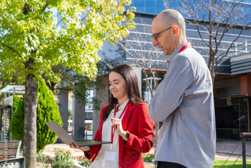 Business colleagues collaborating over a laptop outdoors, discussing a project beside a modern office building