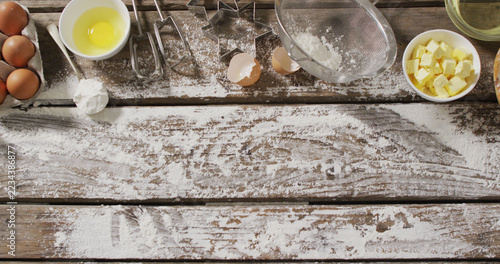Image of baking ingredients and tools lying on wooden surface with flour