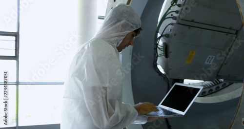 Scientist in a clean suit analyzes data on a laptop in a lab