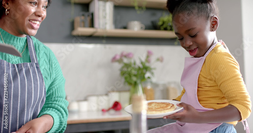 Happy african american mother and daughter wearing aprons and making pancakes
