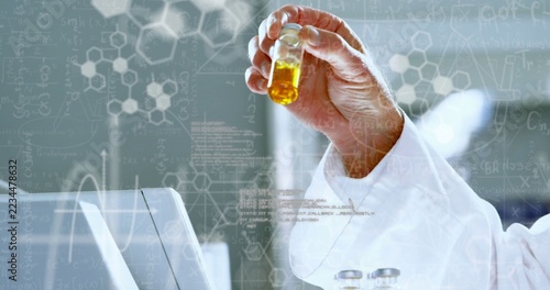 Holding hand in white lab coat, inspecting yellow vial at bench with laptop overlays, copy space