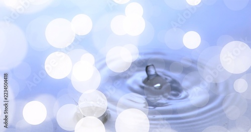 Forming single water droplet creating small splash and ripples on studio basin, with bokeh