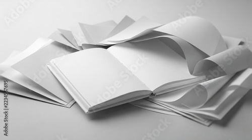 Floating sheets of deckle edge paper around open empty textbook concept of creativity