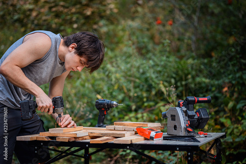 Obraz na plátně Focused guy fastening wooden planks with screws and a power tool in the garden